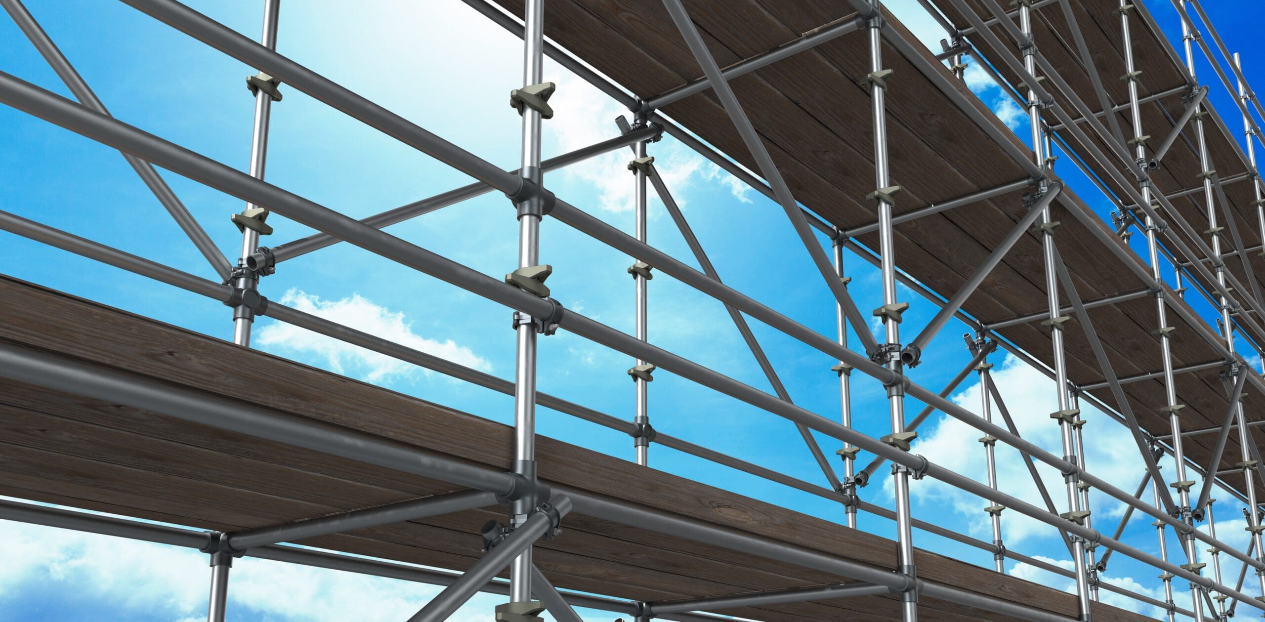 A close-up view of a metal scaffolding structure with wooden planks against a blue sky and scattered white clouds. The geometric pattern of the metal frames creates a visually striking composition.